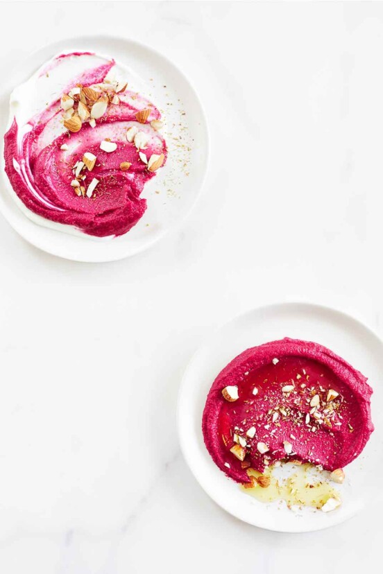 Two white serving plates with swirls of beet hummus, topped with chopped almonds