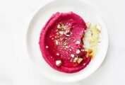 Two white serving plates with swirls of beet hummus, topped with chopped almonds