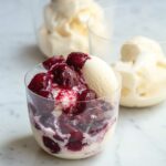 A rocks glass filled with bing cherries with wine syrup and vanilla ice cream