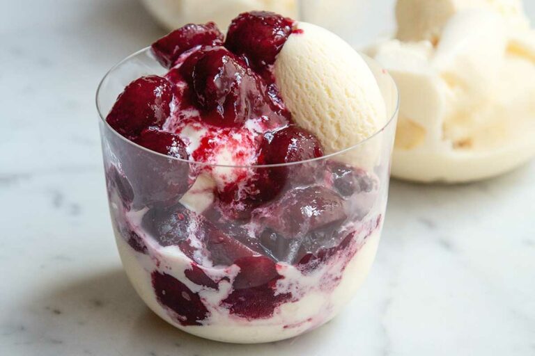 A rocks glass filled with bing cherries with wine syrup and vanilla ice cream