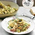 Floral pasta bowl, filled with crab pasta, sprinkled with parsley and Parmesan. A cheese grater and larger bowl in the background.