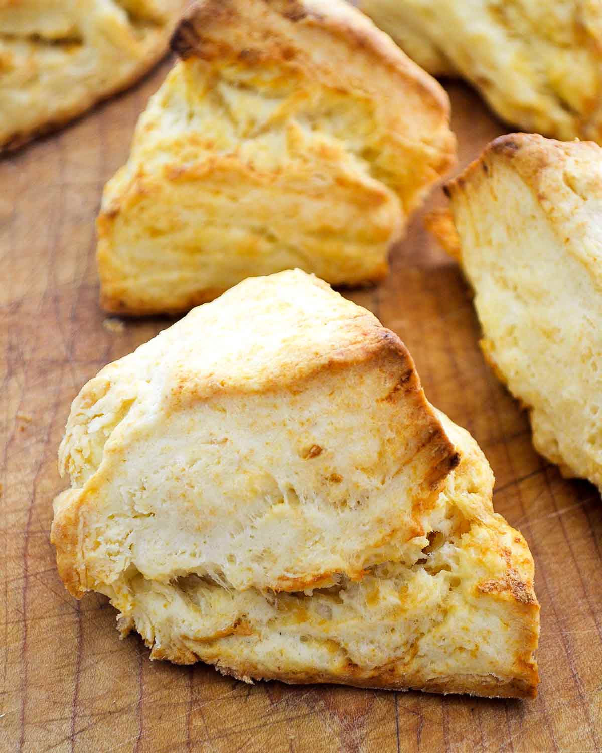 Five irregularly shaped cheddar biscuits with gold edges, on a wooden cutting board.