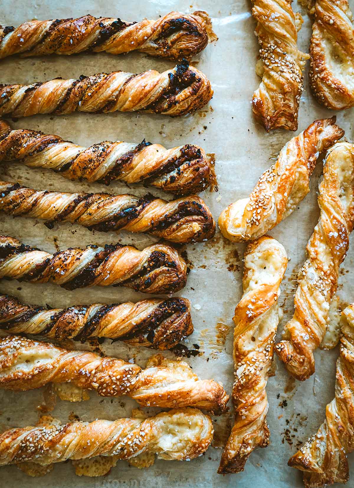 Various filled puff pastry twists lying on a sheet of parchment paper.