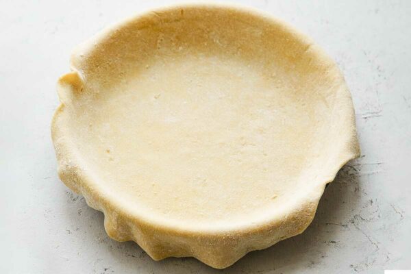 Empty pie crust in a pie plate, with kitchen shears next to it.