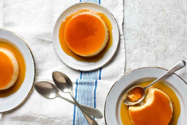 Three plates, each with a creme caramel on them with spoons resting on the side.