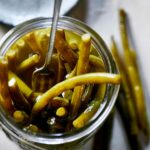 Close-up looking into a mason jar full of pickled green beans and pickling liquid, with a fork.