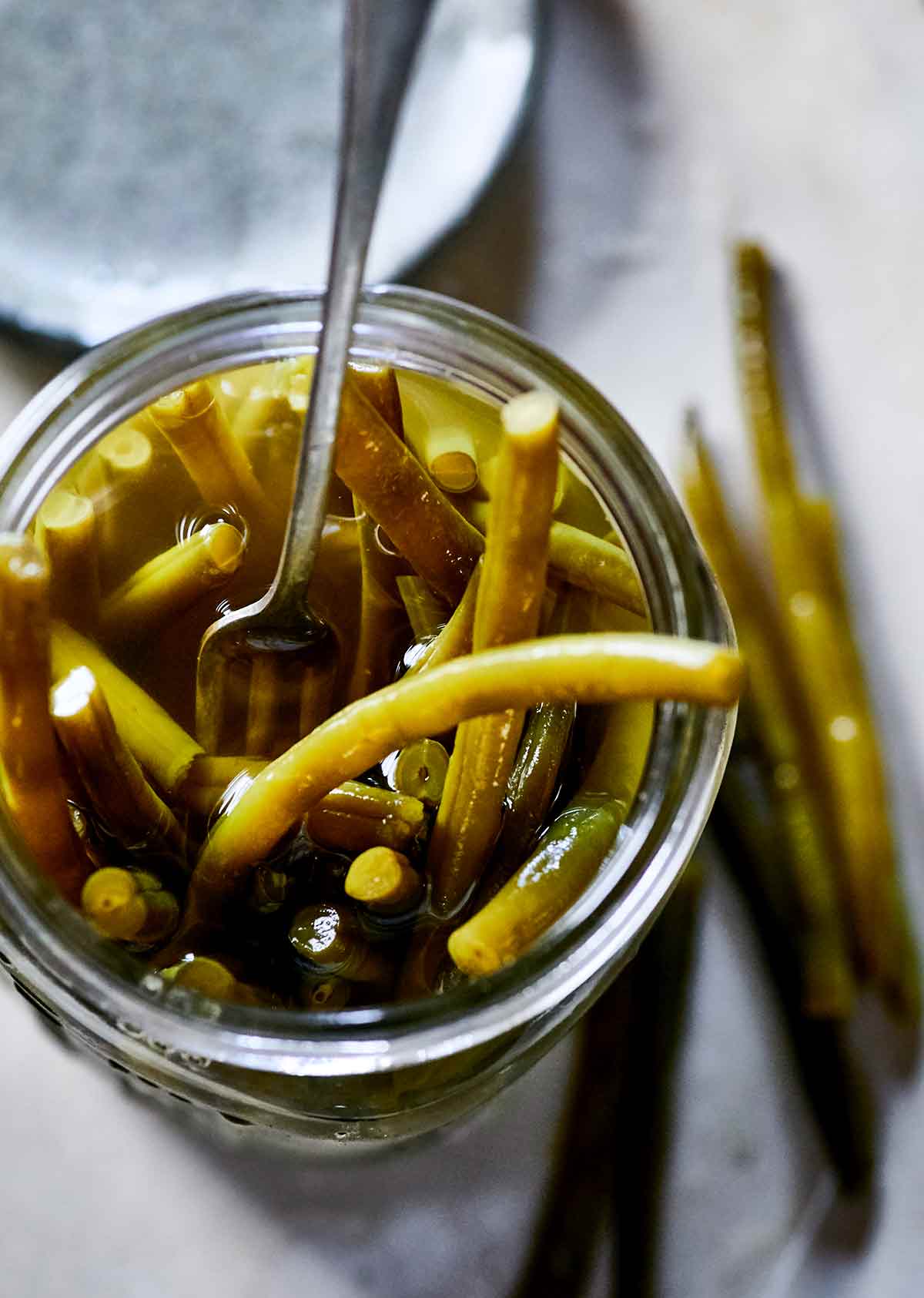 Close-up looking into a mason jar full of pickled green beans and pickling liquid, with a fork.