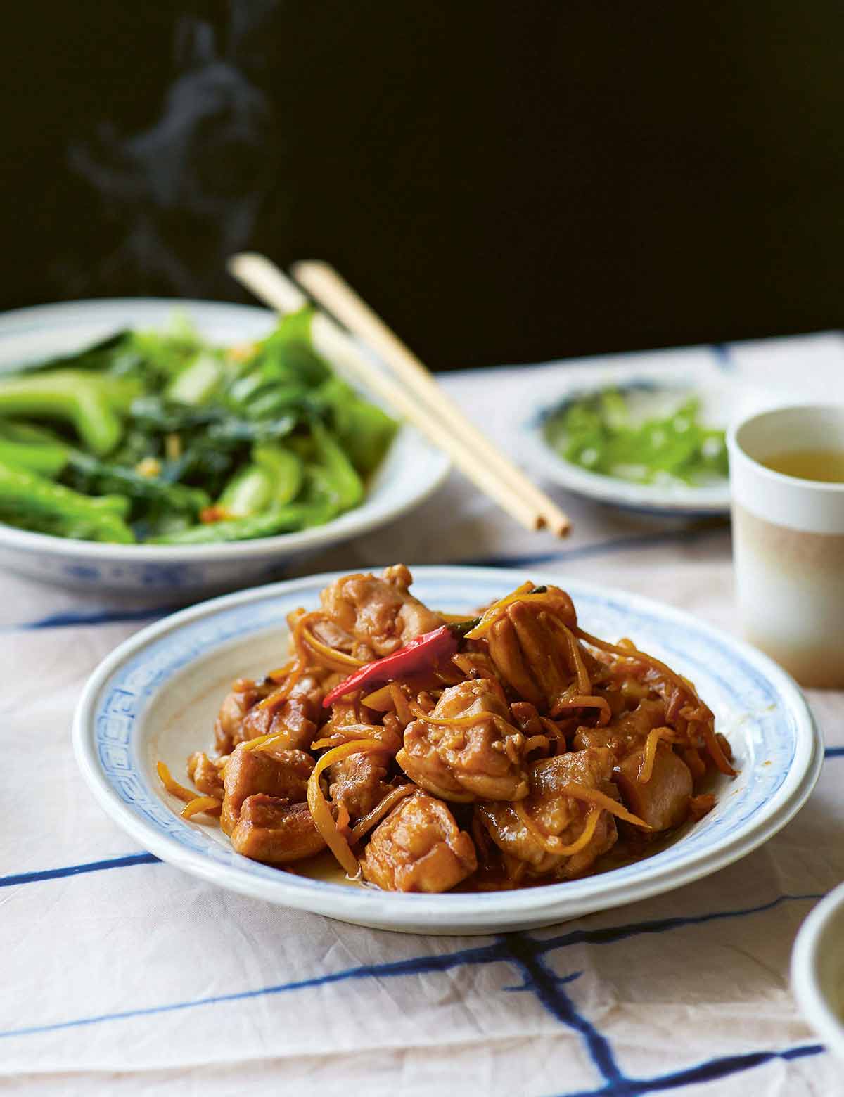 A blue and white dish filled with sauced chicken and julienned ginger, topped with a red chile.