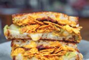 A gray plate with a grilled cheese with Doritos, bacon, and guacamole.