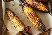 Three cobs of grilled corn with husks attached, lying on a metal sheet pan with parchment paper.Three cobs of grilled corn with husks attached, lying on a metal sheet pan with parchment paper.