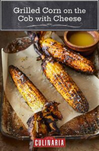 Three cobs of grilled corn with husks attached, lying on a metal sheet pan with parchment paper.