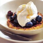 A white bowl with a slice of grilled pineapple, topped with vanilla mascarpone, rum glaze, and fresh blueberries.