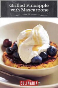 A white bowl with a slice of grilled pineapple, topped with vanilla mascarpone, rum glaze, and fresh blueberries.