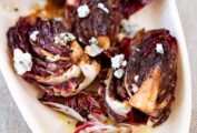 A white platter, piled with quartered grilled radicchio topped with crumbled Gorgonzola cheese.