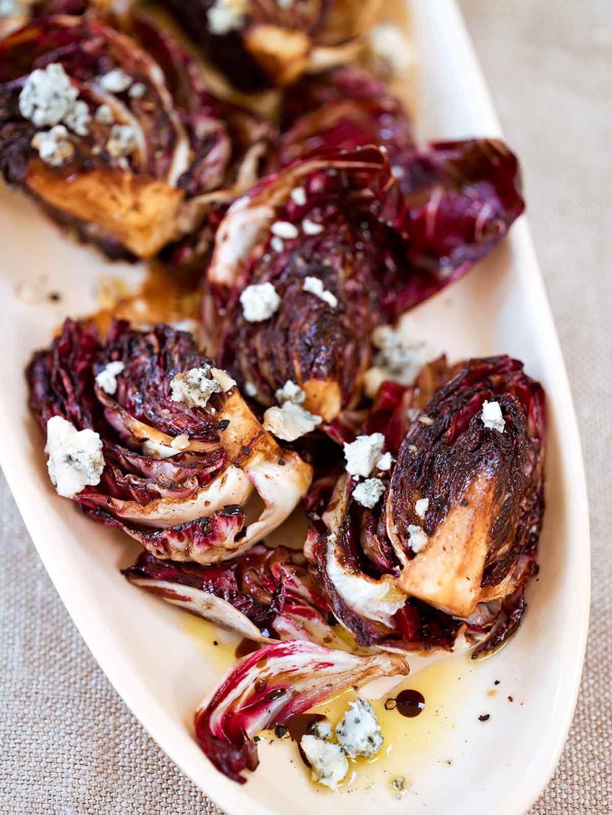 A white platter, piled with quartered grilled radicchio topped with crumbled Gorgonzola cheese.