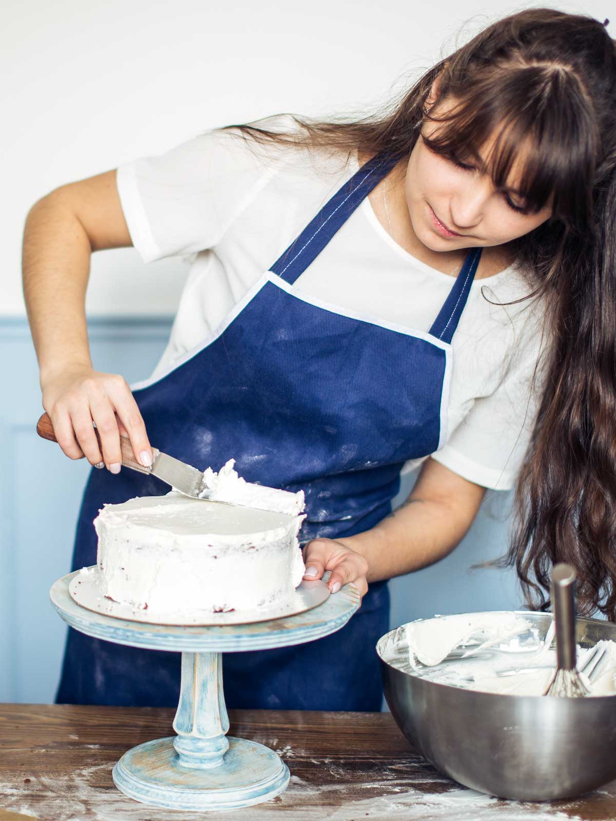 A person applying a thick layer of frosting on a cake