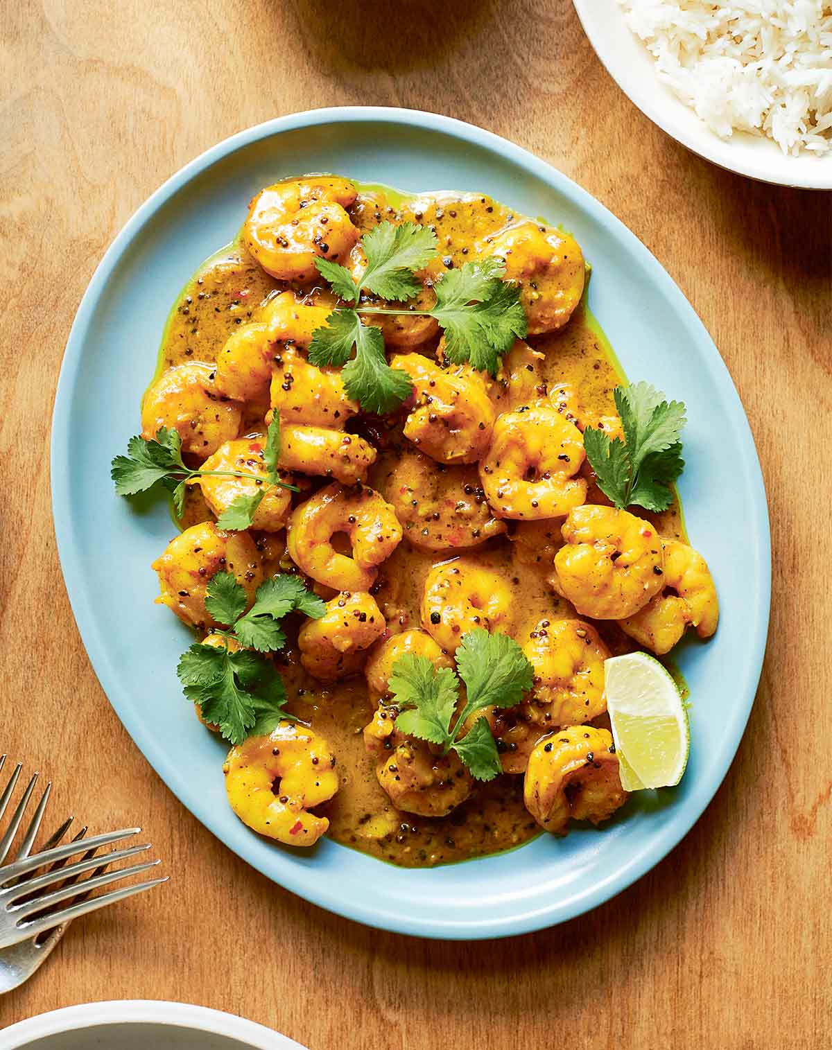 A pale blue platter, filled with fried shrimp in a deep orange sauce flecked with spices and garnished with fresh cilantro leaves.