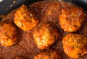 A pan full of turkey meatballs with tomato sauce, beside a chopping board with Parmesan and a bowl of parsley.