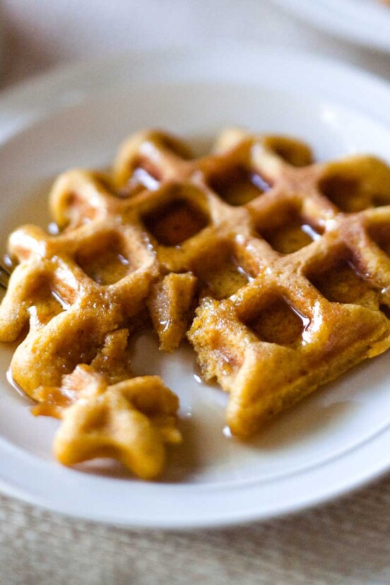 A maple oat waffles lying on a white plate with a fork and syrup in all the pockets.