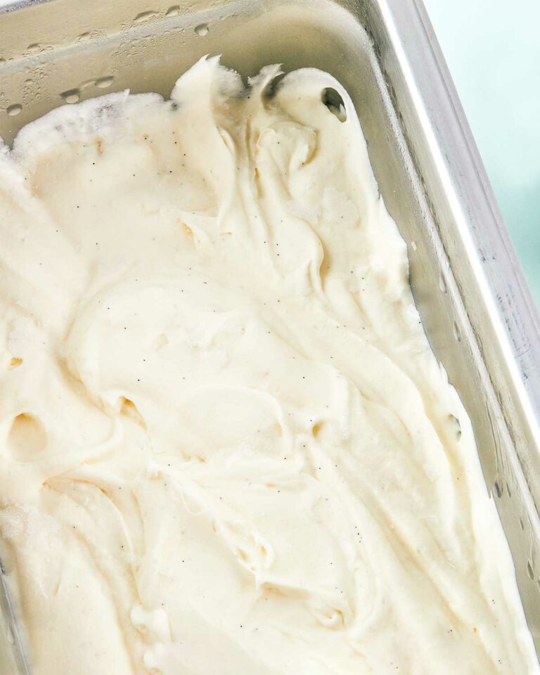 A close-up of vanilla ice cream in a metal pan on a blue background.