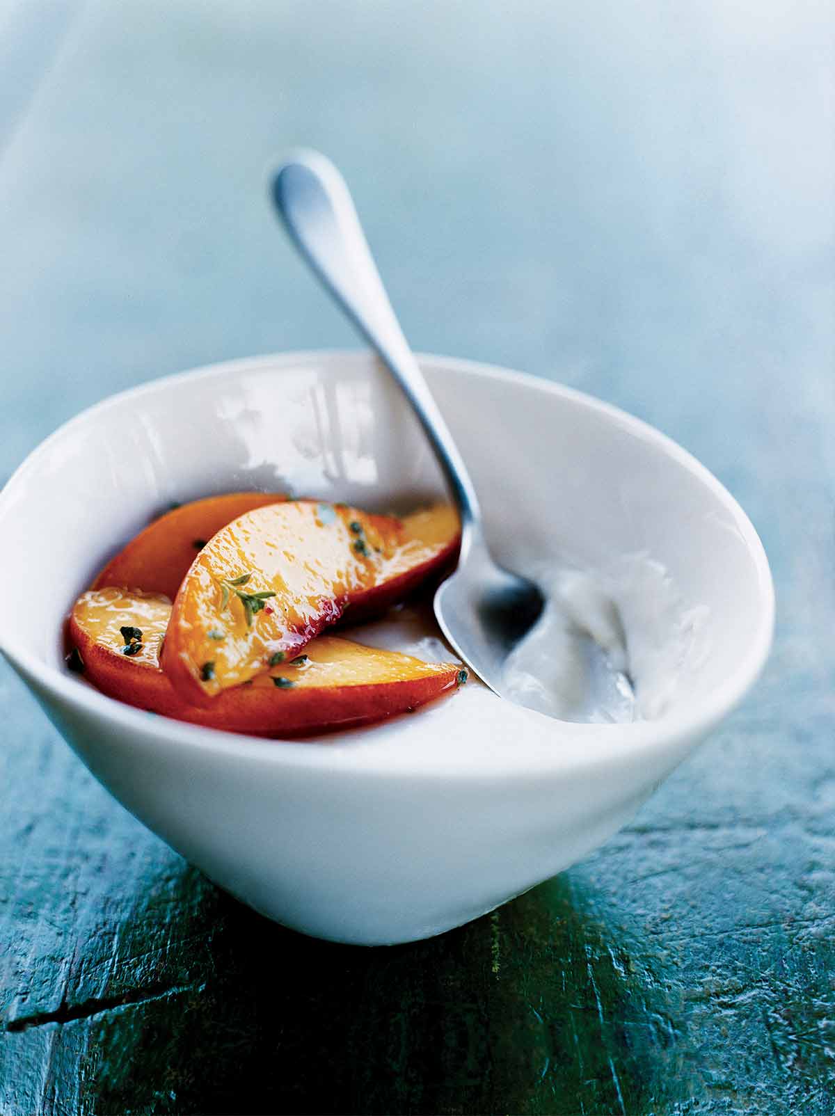 En vit skål fylld med pannacotta med persikor, garnerad med timjan och en sked vilande inuti.
