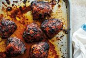 A sheet pan with 9 chicken thighs covered in a deep reddish sauce, blackened in spots.