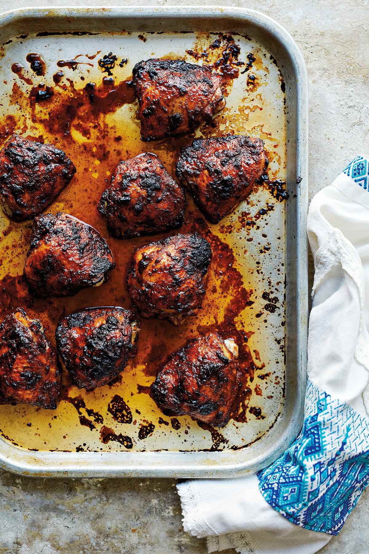 A sheet pan with 9 chicken thighs covered in a deep reddish sauce, blackened in spots.