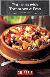 A terracotta dish filled with potatoes, feta, black olives, and tomatoes.
