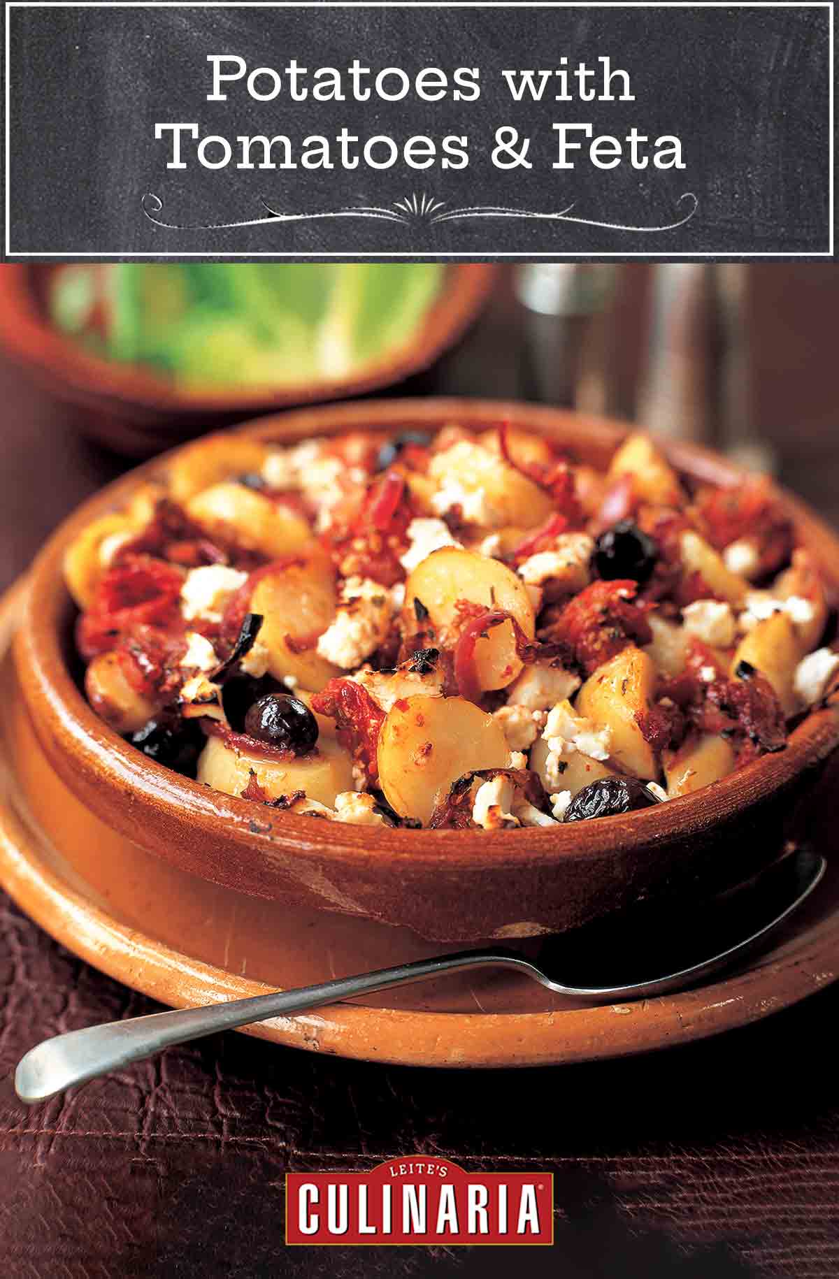 A terracotta dish filled with potatoes, feta, black olives, and tomatoes.