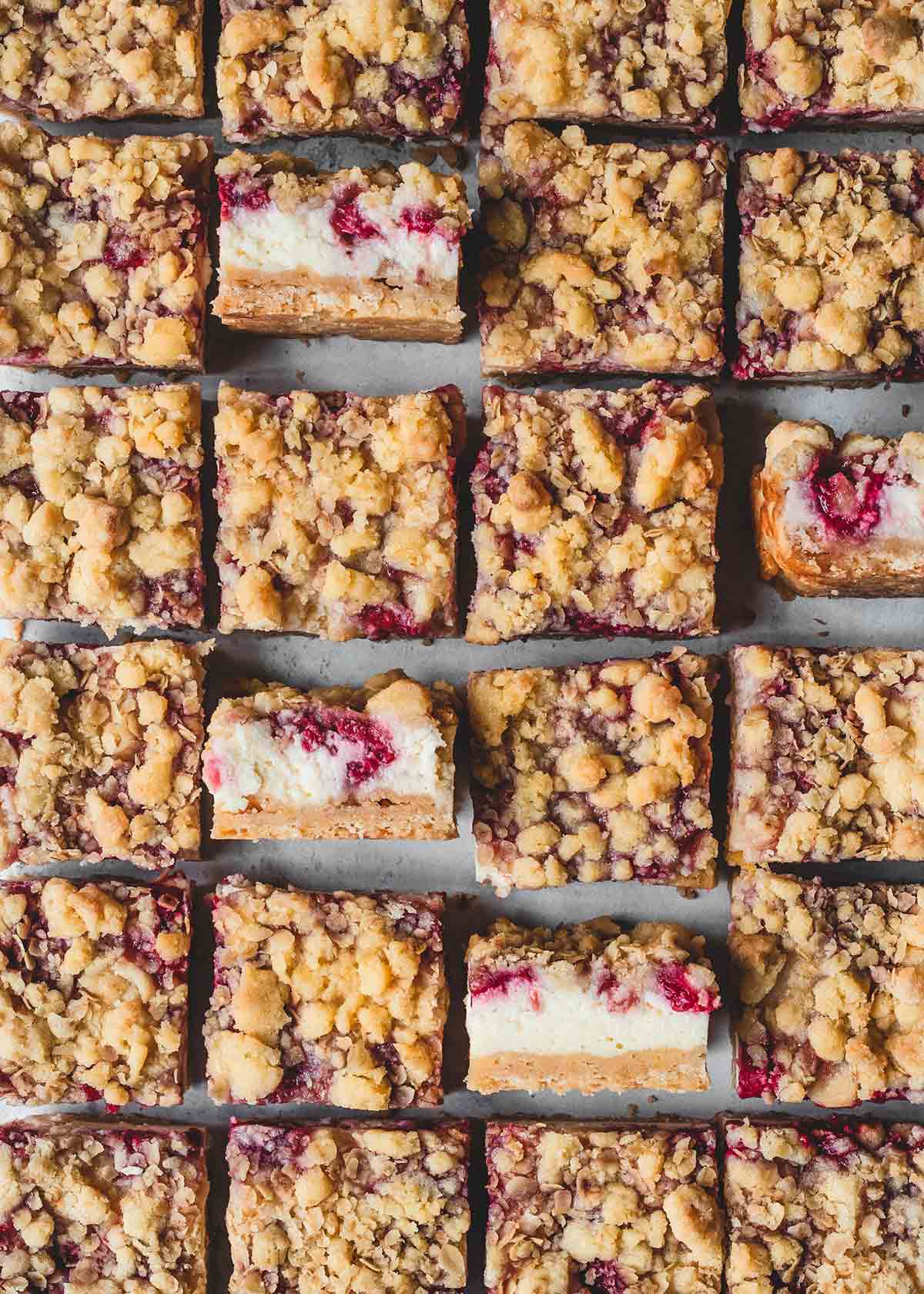 Twenty-four raspberry cheesecake streusel bars on parchment paper.