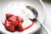 A bowl of rice pudding with a spoon and a scoop of halved strawberries and juice