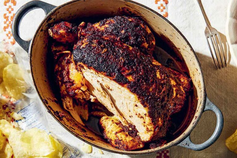 A cast-iron Dutch oven filled with a deeply roasted chicken, flanked by a bag of potato chips.
