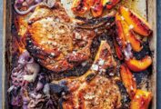 A rimmed sheet pan with roast pork chops with peaches and cooked red onion.