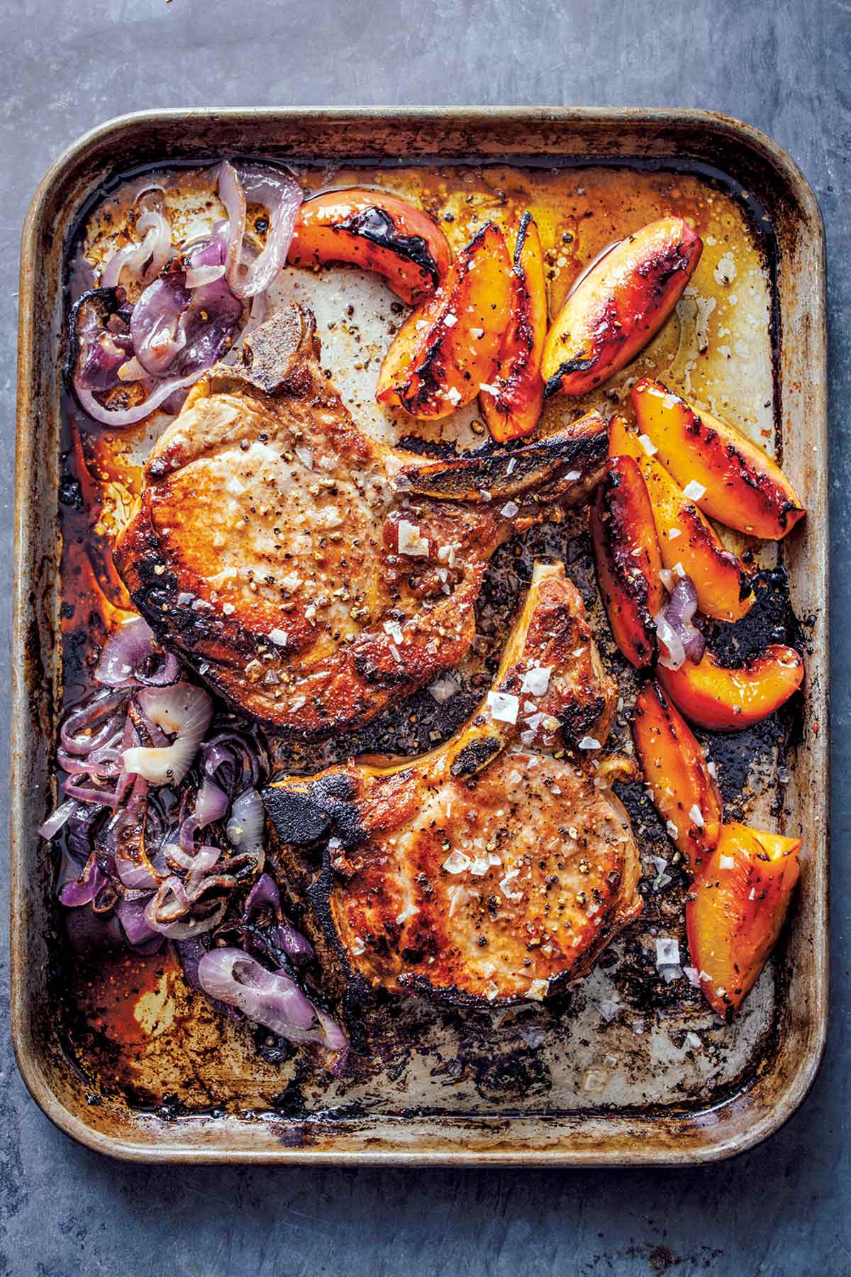 A rimmed sheet pan with roast pork chops with peaches and cooked red onion.