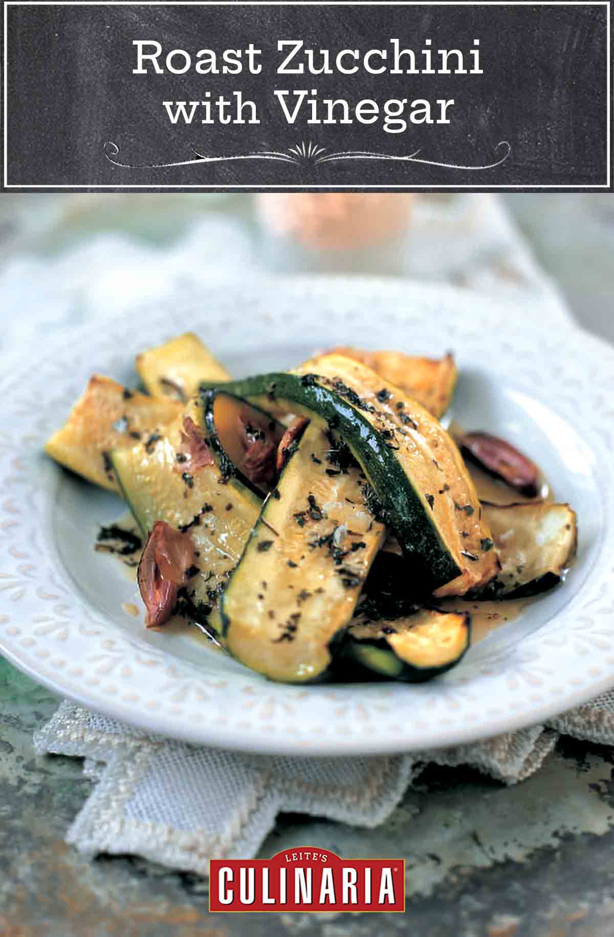 A white plate filled with slices of roasted zucchini, olive oil, dark roasted cloves of garlic, and mint.