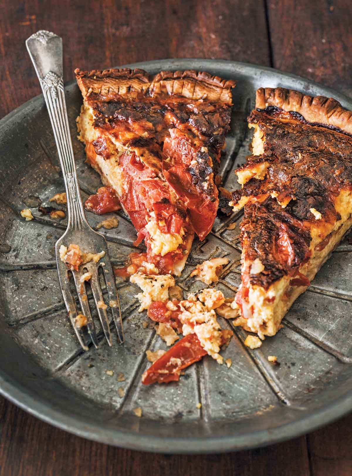 A metal pie plate with two slices of roasted tomato quiche, some crumbs of crust and a fork.