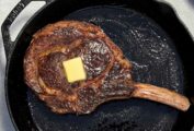 A large rib eye steak with a pat of butter on top, in a cast iron pan.
