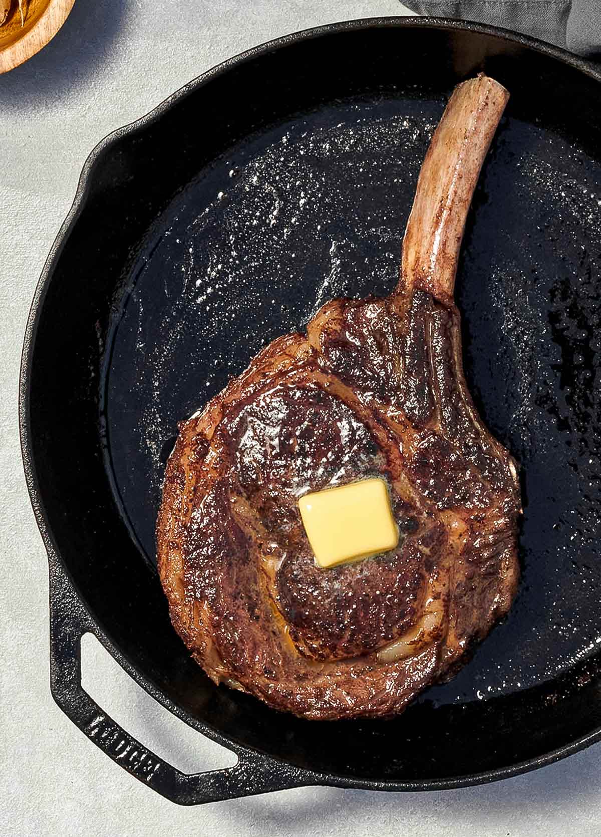 En stor rib eye steak med en klick smör på toppen, i en gjutjärnspanna.