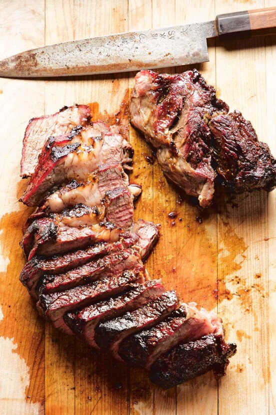 A cutting board and knife, topped with a large piece of grilled beef, sliced into strips.