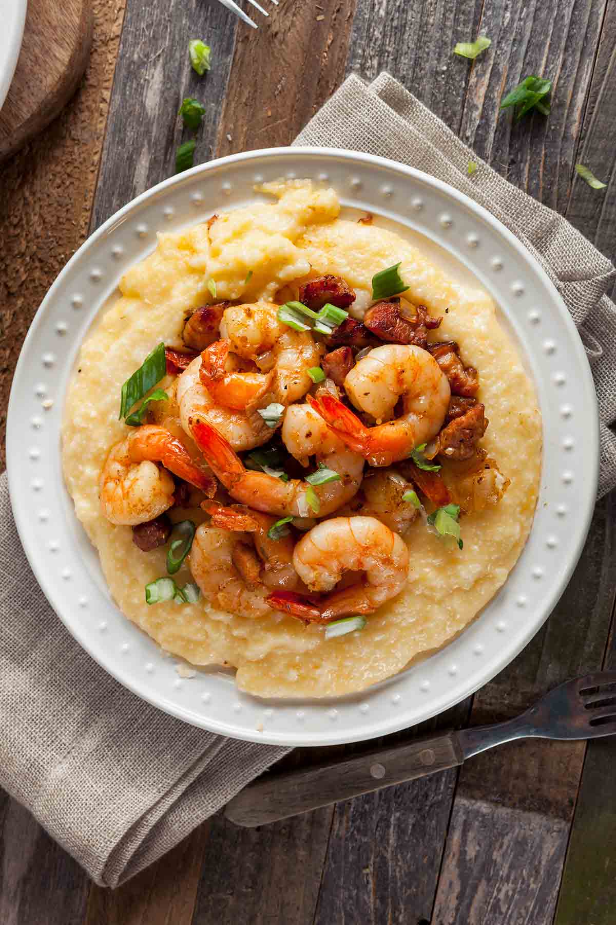 A white plate filled with cheesy shrimp and grits with bacon
