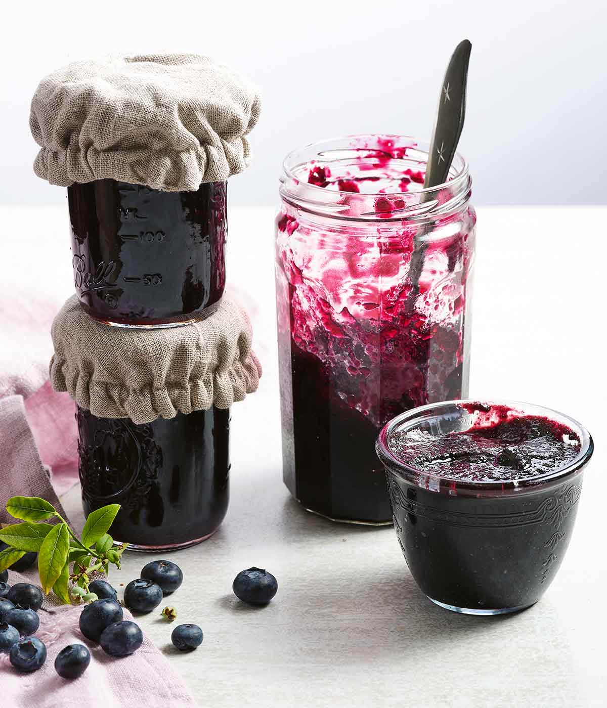 Four small jars of blueberry jam, one is half gone with a spoon in it.