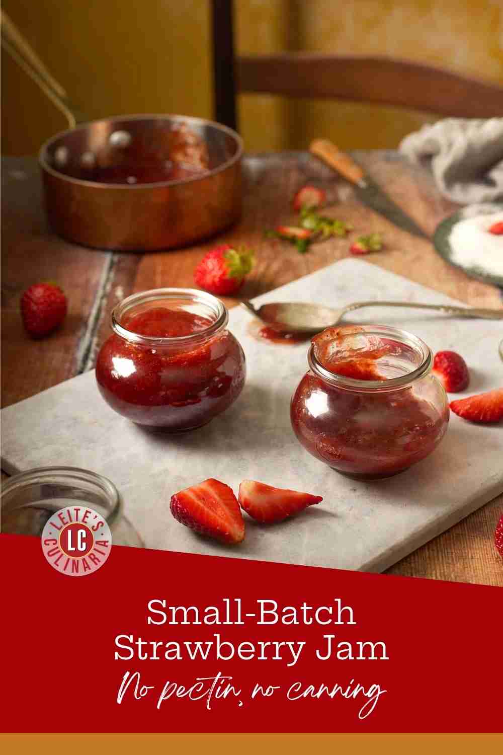 Glossy red strawberry jam in glass jars on a marble board with fresh sliced berries.