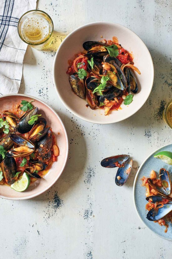Three bowls of smoky chile and tomato mussels, on a table flanked by a glass of beer and a few empty mussel shells.
