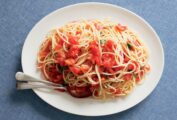 An oval platter topped with spaghetti with raw tomatoes and a couple of spoons on the side.