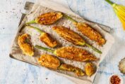 A large pan covered with parchment paper and 8 deep fried zucchini flowers, sprinkled with lemon zest, salt, and chile flakes.