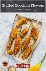 A large pan covered with parchment paper and 8 deep fried zucchini flowers, sprinkled with lemon zest, salt, and chile flakes.