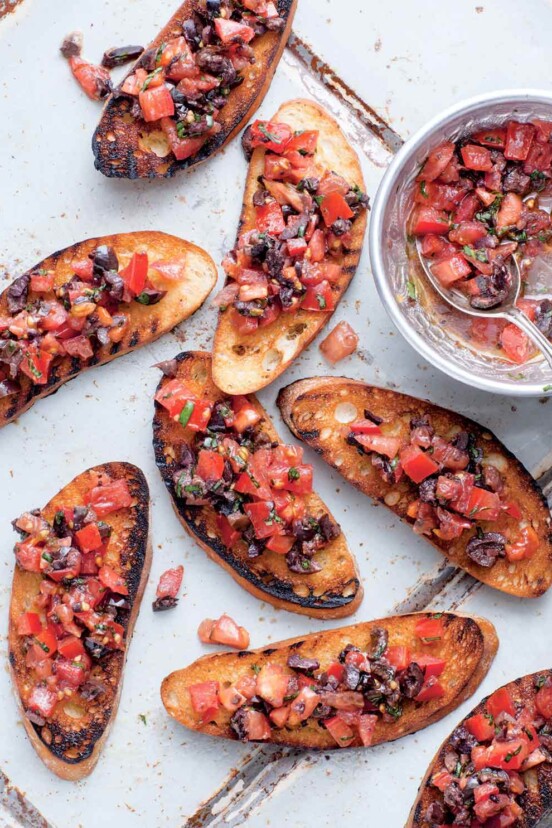 Eight slices of tomato bruschetta with a bowl of tomato bruschetta on the side.