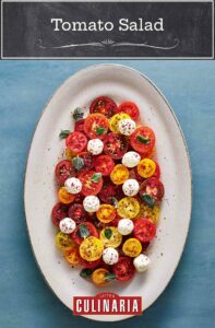 A large white platter filled with halved various colored cherry tomatoes, labneh balls, olive oil, and a sprinkle of spices.