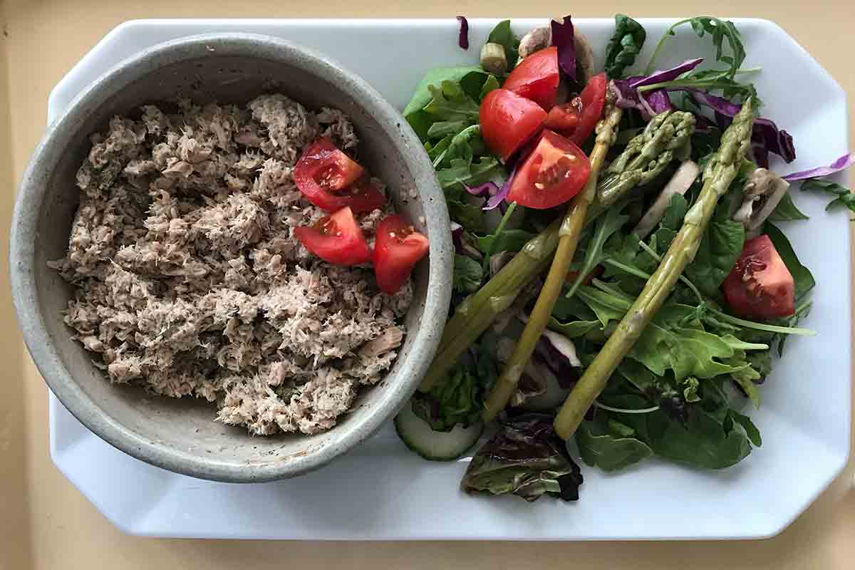A colorful Tuna Salad with Capers, Yogurt and Za'atar on a white serving platter with tuna in a bowl on the left and lettuce, tomatoes and asparagus on the right.