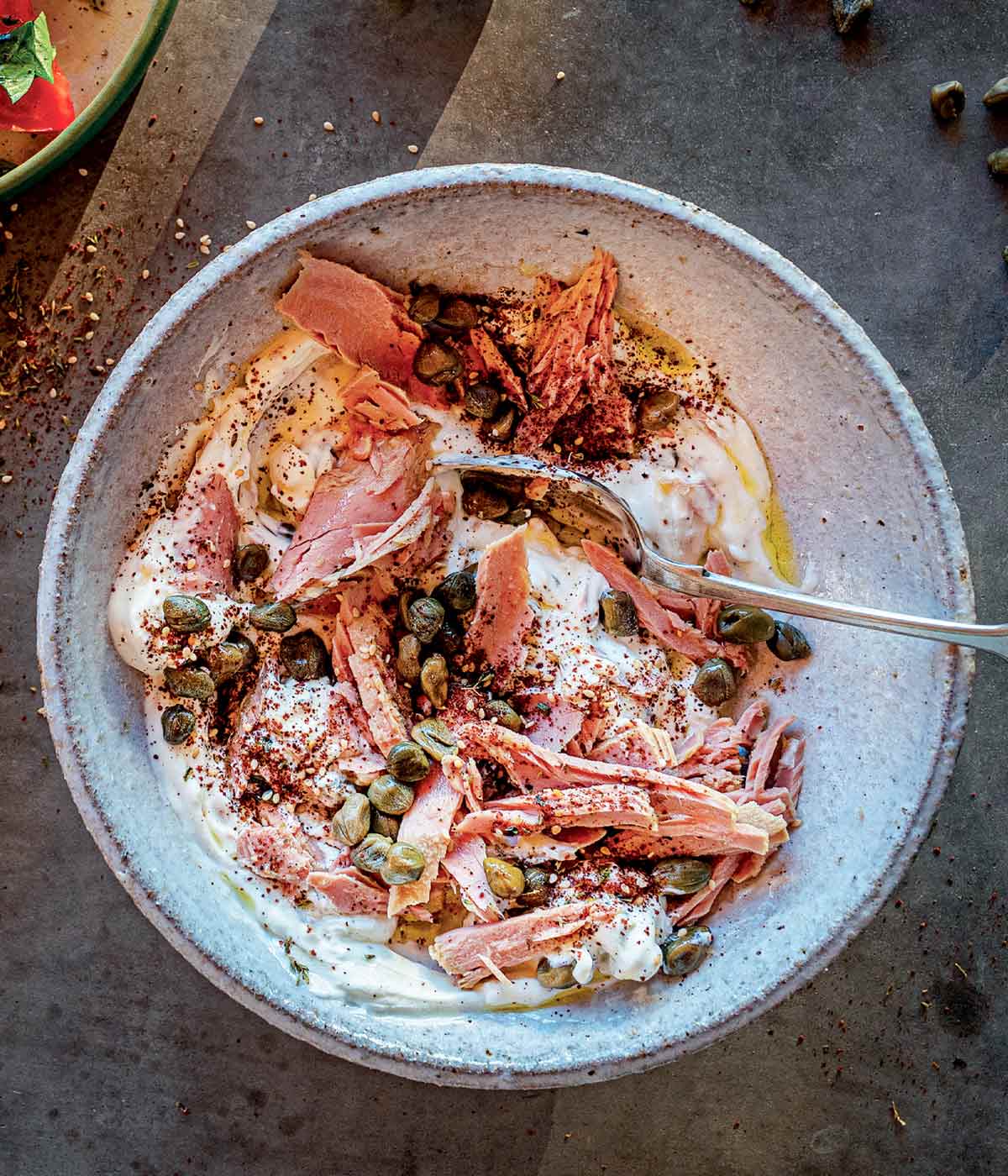 A pottery bowl filled with tuna salad, yogurt, olive oil, capers, and za'atar.